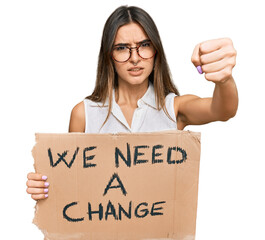 Young hispanic woman holding we need a change banner annoyed and frustrated shouting with anger,...