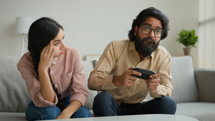Diverse multiethnic couple at home bored angry arabian woman offend on husband addicted playing console video game with joystick focused indian man gamer ignoring wife play tv gamepad gaming addiction - obrazy, fototapety, plakaty