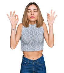 Young blonde girl wearing casual style with sleeveless shirt relax and smiling with eyes closed doing meditation gesture with fingers. yoga concept.