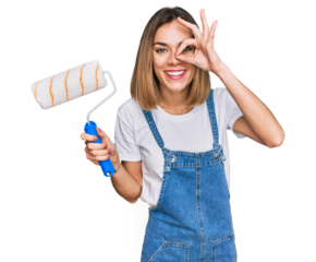 Young blonde girl holding roller painter smiling happy doing ok sign with hand on eye looking through fingers