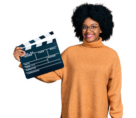 Young african american woman holding video film clapboard looking positive and happy standing and...