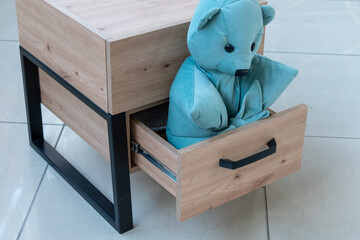 Cabinet furniture. Soft blue bear toy in opened drawer of wooden bedside table close-up
