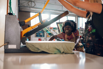 Interracial print shop workers working with heating press at facility.