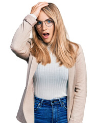 Young blonde woman wearing business shirt and glasses surprised with hand on head for mistake, remember error. forgot, bad memory concept.