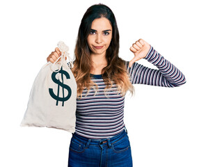 Beautiful hispanic woman holding dollars bag with angry face, negative sign showing dislike with...
