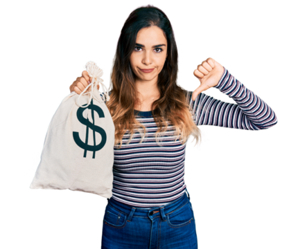 Beautiful hispanic woman holding dollars bag with angry face, negative sign showing dislike with thumbs down, rejection concept