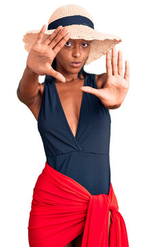 Young african american woman wearing swimsuit and summer hat doing frame using hands palms and fingers, camera perspective