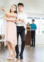 Fototapeta na wymiar Enthusiastic young couple, elegant Latin American guy and dark-haired girl in formal wear, performing kizomba in studio, demonstrating dance characteristic sensual and connected movements..