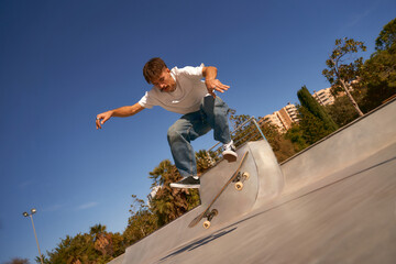 Active skateboarder jumping and performing a trick in a ramp of a skate park