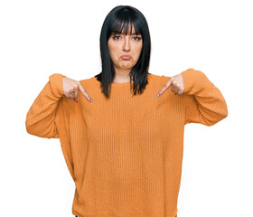 Young hispanic woman wearing casual clothes pointing down looking sad and upset, indicating...