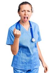 Young beautiful blonde woman wearing doctor uniform and stethoscope angry and mad raising fist...