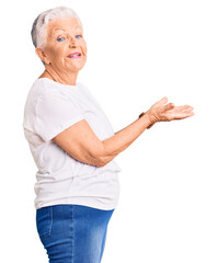 Senior beautiful woman with blue eyes and grey hair wearing casual white tshirt pointing aside with...