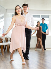 Happy girl and guy enjoying passionate latin american dancing with male partner in dance hall