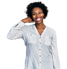 African american woman with afro hair wearing casual white t shirt smiling doing phone gesture with...