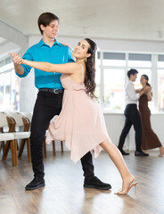 Girl and guy in festive clothes dancing slow ballroom dance during group lesson in a choreography...