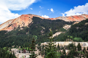 Obraz premium Red Mountain peaks and forest summer landscape of pine trees in the San Juan Mountains of southwest Colorado, USA with blue sky and white clouds.