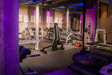 Modern gym with strength training equipment like leg curl machine, dumbbell rack, and cable...
