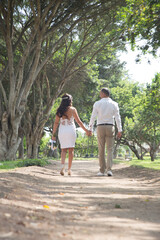 Young couple walking together and holding hands after they got married through a park