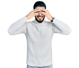 Young arab man with beard wearing elegant turtleneck sweater and glasses covering eyes with hands...