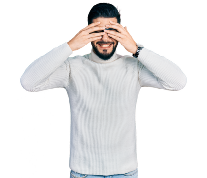 Young arab man with beard wearing elegant turtleneck sweater and glasses covering eyes with hands smiling cheerful and funny. blind concept.
