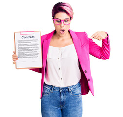 Young beautiful woman with pink hair holding clipboard with contract document pointing down with...