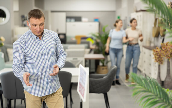 Male customer choose dining table desk in furniture store showroom. Man runs hand over smooth surface, imagining how it would look in dining room