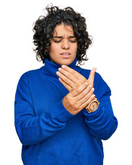 Young hispanic woman with curly hair wearing turtleneck sweater suffering pain on hands and...