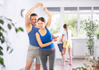Smiling mother and father learning dynamic boogie-woogie in pair in dance studio during family class