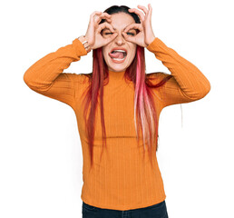 Naklejka premium Young caucasian woman wearing casual clothes doing ok gesture like binoculars sticking tongue out, eyes looking through fingers. crazy expression.