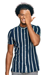 African american man with afro hair wearing casual clothes covering one eye with hand, confident smile on face and surprise emotion.