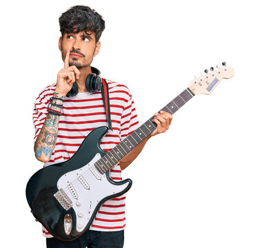 Young hispanic man playing electric guitar serious face thinking about question with hand on chin, thoughtful about confusing idea