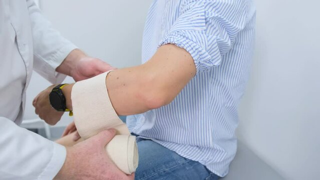 The traumatologist carefully removes the elastic bandage from the young man's arm, helping to recover from injury.