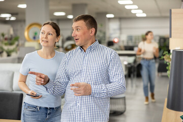 Positive adult couple, woman and man visiting store in search of new furnishings for apartment,...