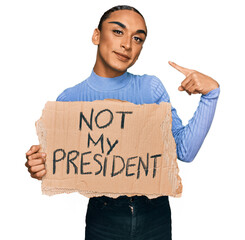 Hispanic transgender man wearing make up and long hair holding not my president protest banner...