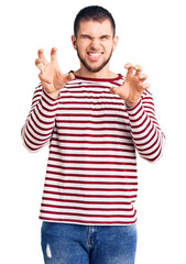 Young handsome man wearing striped sweater smiling funny doing claw gesture as cat, aggressive and sexy expression