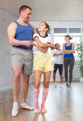 Cheerful middle-aged man practicing active dance in pair with his tween daughter during family...
