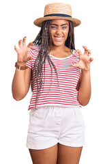 Obraz na płótnie Canvas Young african american woman with braids wearing summer hat smiling funny doing claw gesture as cat, aggressive and sexy expression