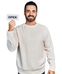 Young hispanic man with beard holding open banner looking positive and happy standing and smiling...