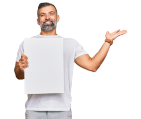 Middle age handsome man holding blank empty banner celebrating victory with happy smile and winner expression with raised hands