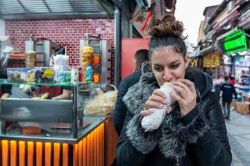 Obraz premium Experiencing street food. A young woman is on vacation and tries out street food, in a tourist side street at a local street vendor selling food. Fast food