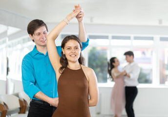 Positive elegant couple, young girl and guy in formal wear dancing sensual Latin dance bachata in sunlit choreography studio. Active lifestyle of youth.. - obrazy, fototapety, plakaty