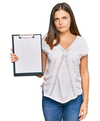Young caucasian woman holding clipboard with blank space thinking attitude and sober expression...