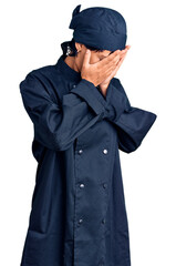 Young brunette woman with short hair wearing professional cook uniform with sad expression covering face with hands while crying. depression concept.