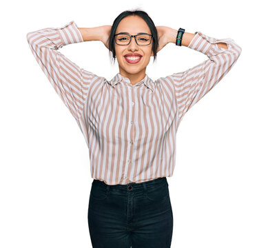 Young hispanic girl wearing casual clothes and glasses relaxing and stretching, arms and hands behind head and neck smiling happy