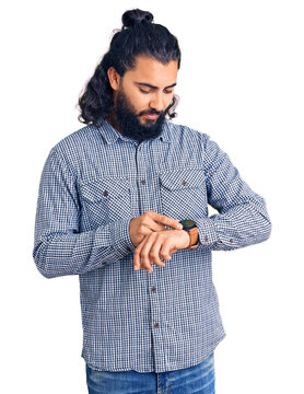 Young arab man wearing casual clothes checking the time on wrist watch, relaxed and confident