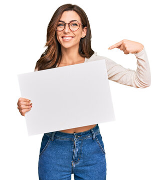 Young brunette woman holding blank empty banner pointing finger to one self smiling happy and proud