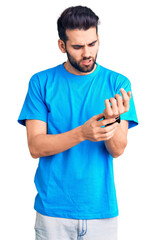 Young handsome man with beard wearing casual t-shirt suffering pain on hands and fingers, arthritis...