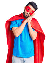 Young handsome man with beard wearing super hero costume sleeping tired dreaming and posing with hands together while smiling with closed eyes.