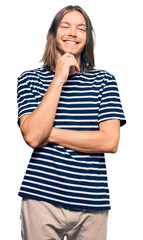 Handsome caucasian man with long hair wearing casual striped t-shirt looking confident at the camera with smile with crossed arms and hand raised on chin. thinking positive.