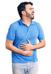 Young hispanic man wearing casual clothes with hand on stomach because nausea, painful disease feeling unwell. ache concept.